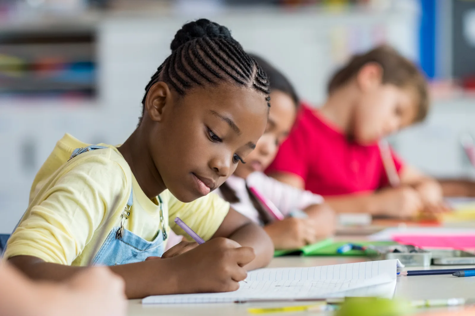 Children at a shared desk, heads down, writing in their notebooks